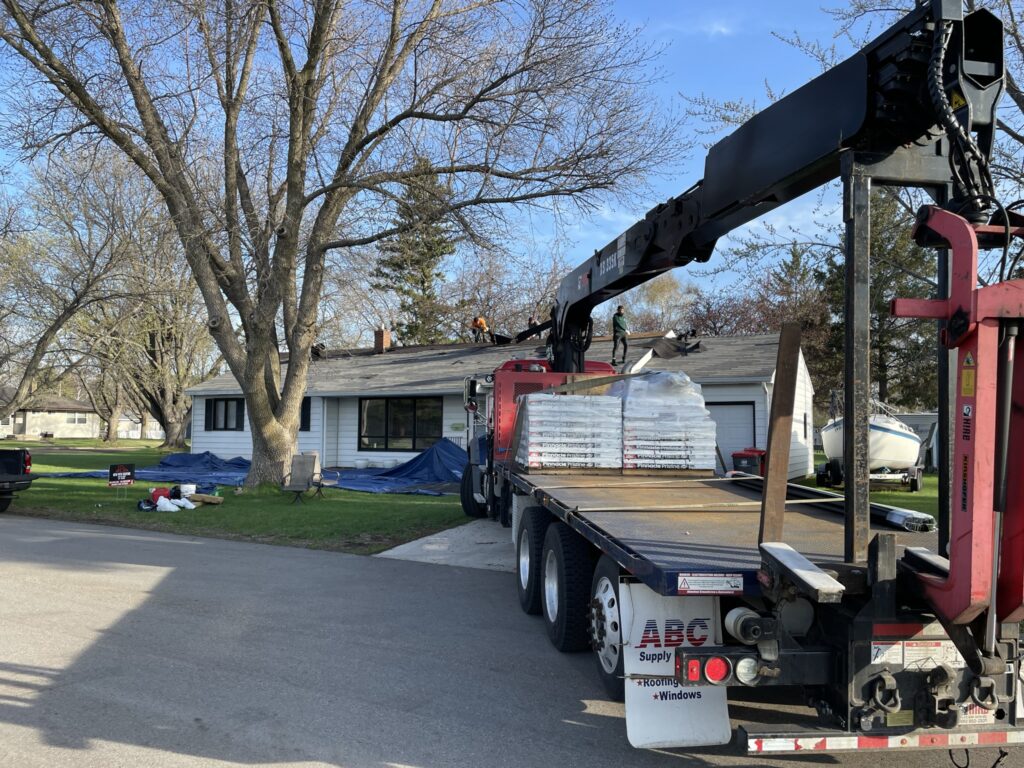 Materials staged and the property protected before work begins — driveway, landscaping, and siding covered so nothing takes damage but the old roof.